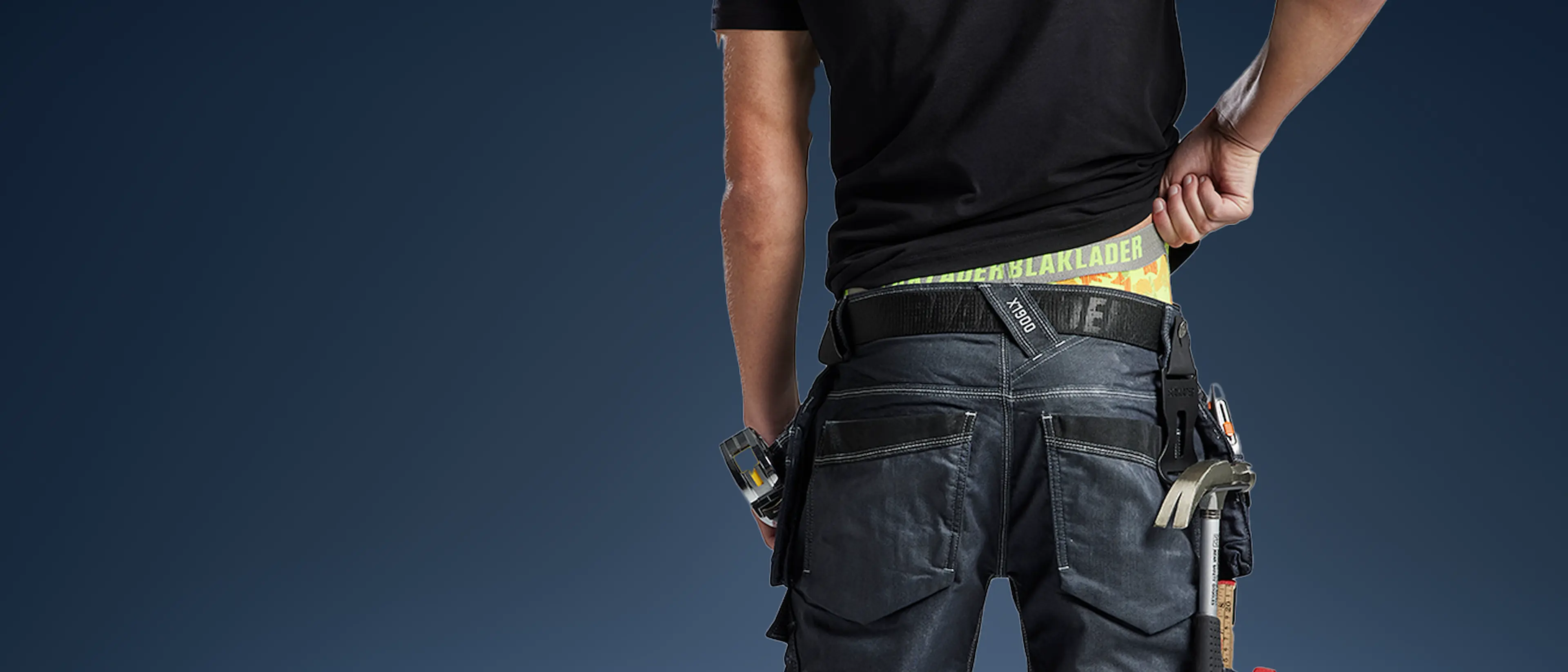 A man showing a glimpse of his camouflage yellow Blåkläder boxers under his craftsman trousers filled with tools
