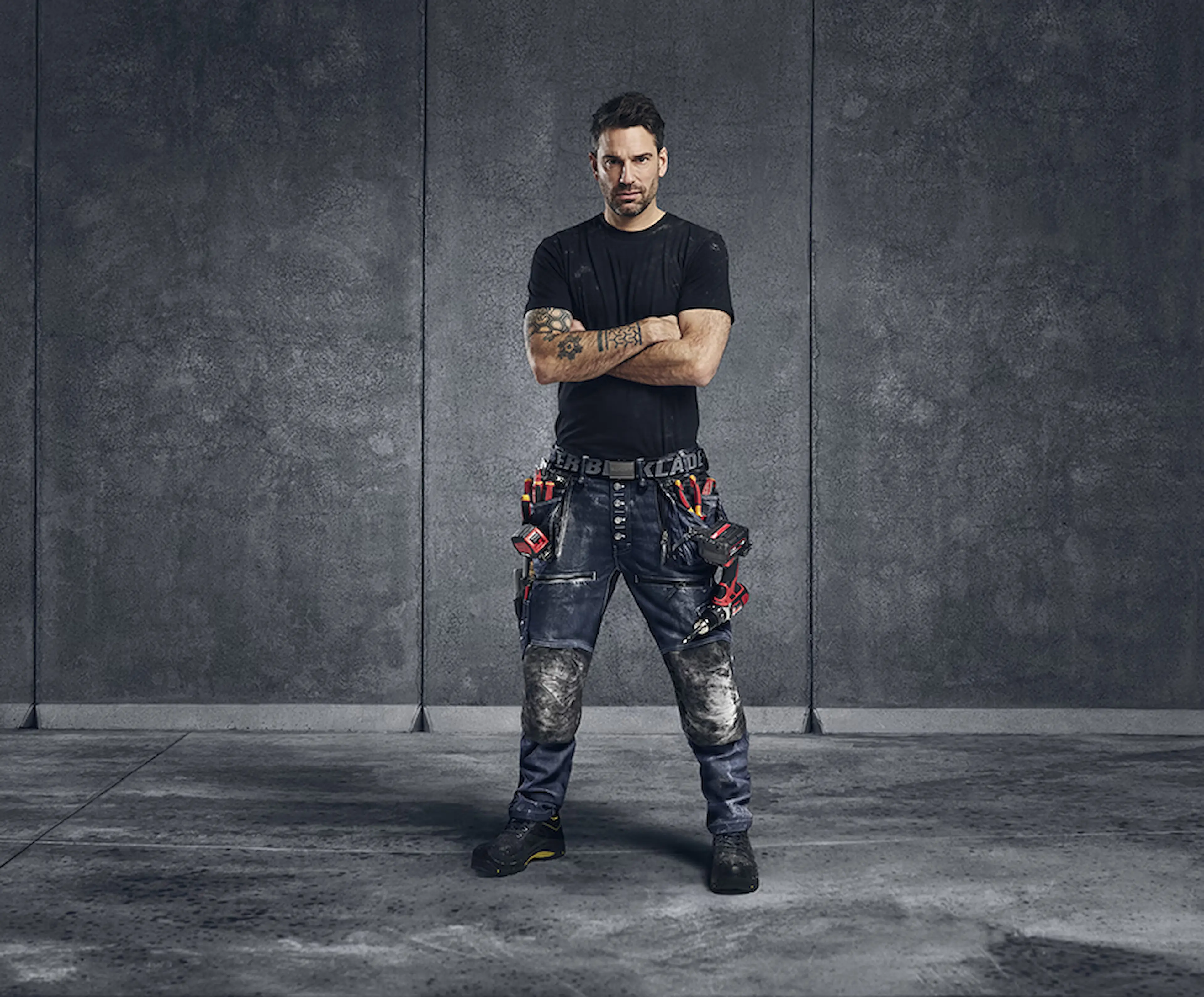 Worker wearing durable work trousers with integrated tool pockets, paired with a basic work shirt—designed for freedom of movement, functionality and everyday durability on the job.