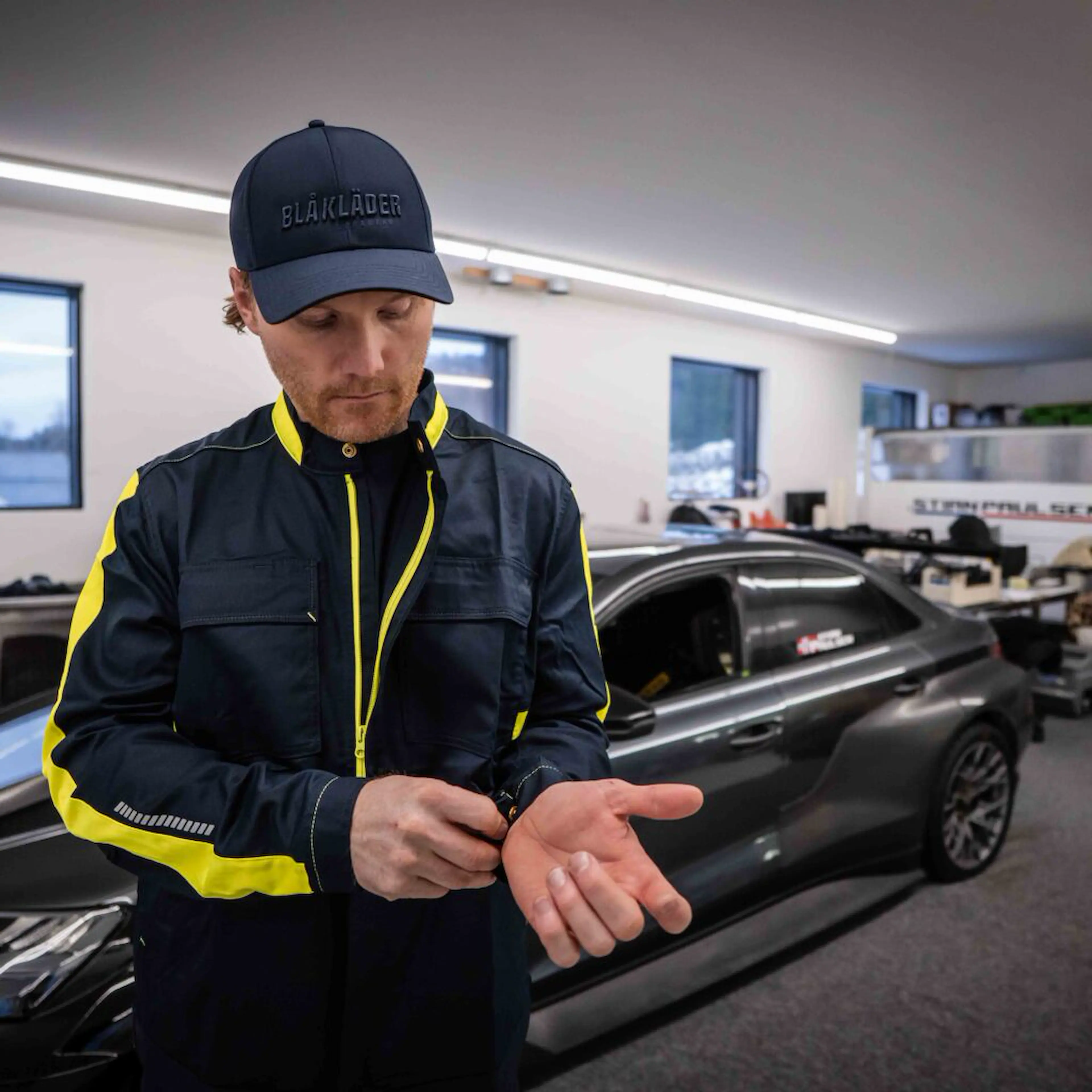 Bilde av Blåkläder-ambassadør Stian Paulsen i garasjen hans, ikledd industrijakke og caps